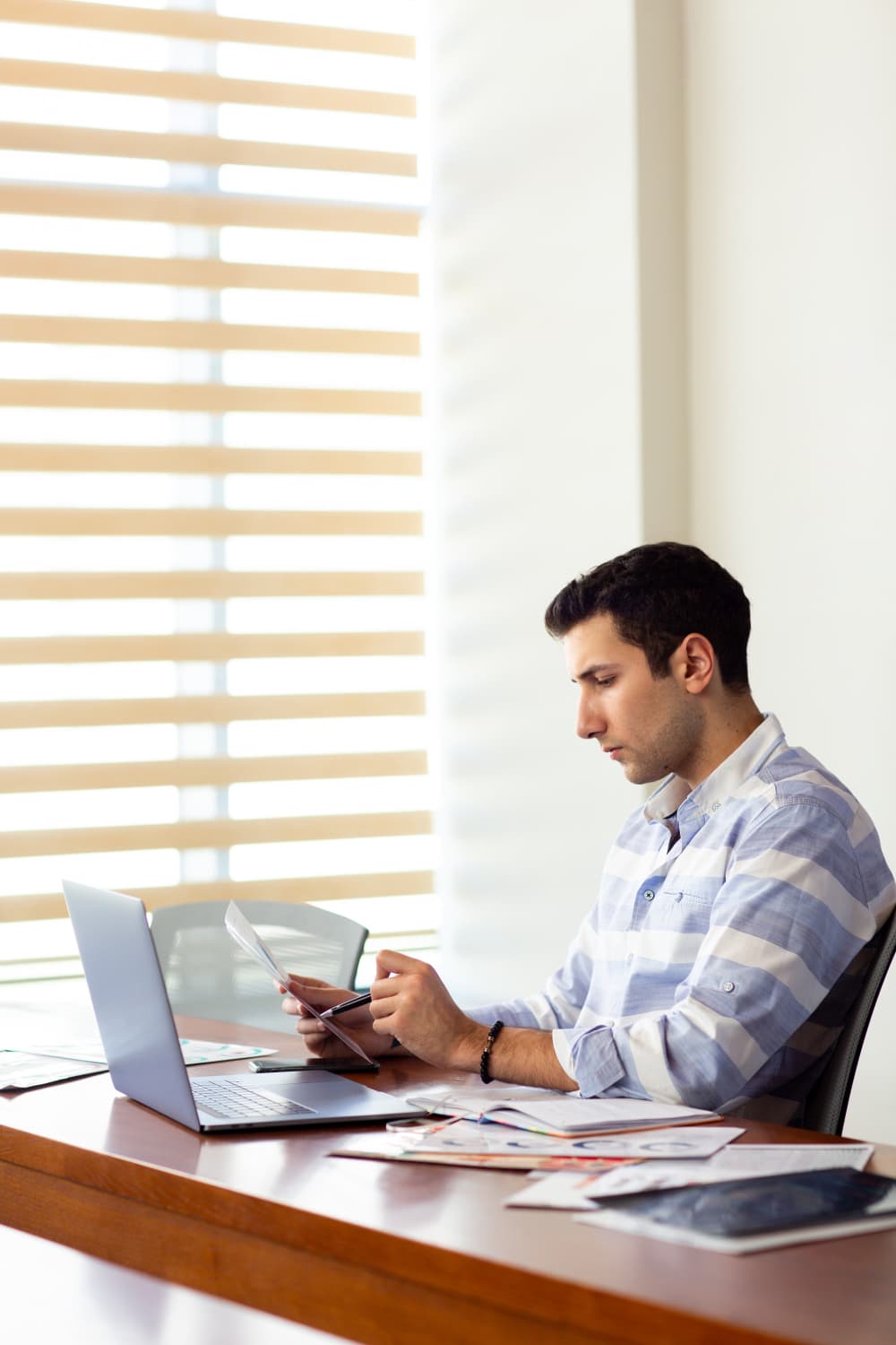 Professional reviewing a document and notes at a desk with a laptop